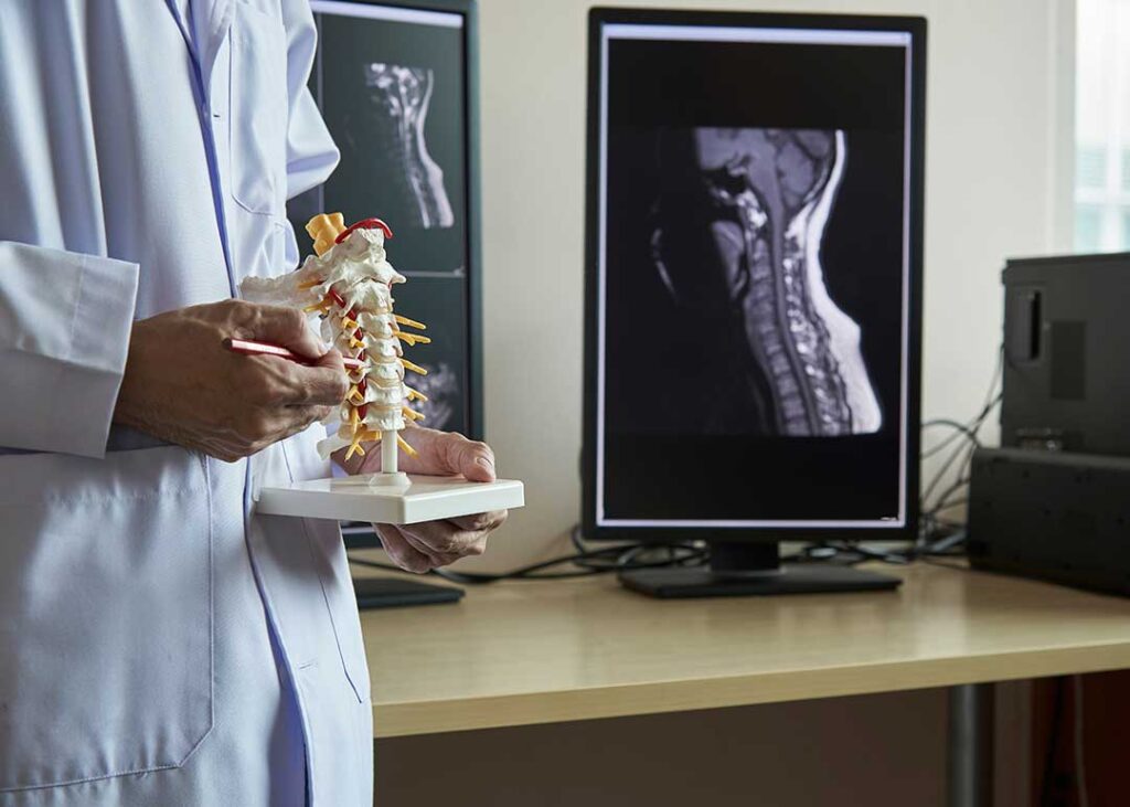 A chiropractor using hands to gently adjust a person's mid-back while the person lies face down on a treatment table.